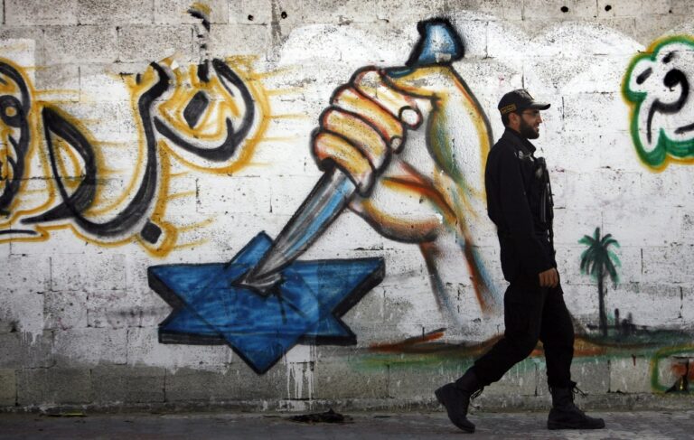 epa02690235 A Palestinian Hamas security man walks next to the mural painted by Hamas members, showing a hand with a dagger stabbing a star of David in the west of Gaza City on 16 April 2011. Reports state that Hamas found the body of the pro-Palestinian Italian activist on 15 April, who was allegedly killed by al Qaeda sympathisers in the Gaza Strip, raising questions about the Islamist group's control over the beleaguered enclave. EPA/ALI ALI