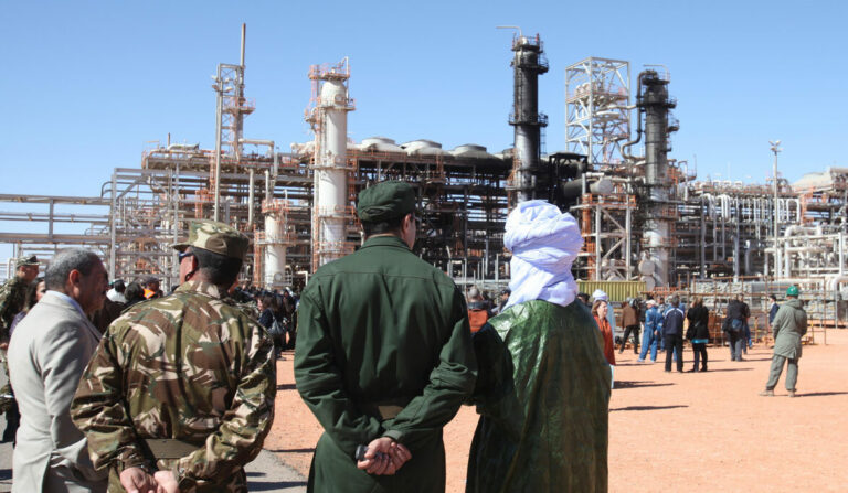 Algerian soldiers and officials stand in front of the gas plant in Ain Amenas, seen in background, during a visit organized by the Algerian authorities for news media, Friday, Jan. 31, 2013. The Algerian gas plant attacked by militants will soon be partially operational, announced its director on Thursday during a tour on the site for local and international media. Lotfi Benadouda, the director of the Ain Amenas plant, which is jointly run by Algeria's Sonatrach, Britain's BP and Norway's Statoil said one of three gas units was only lightly damaged and would be returned to operation soon. (AP Photo)