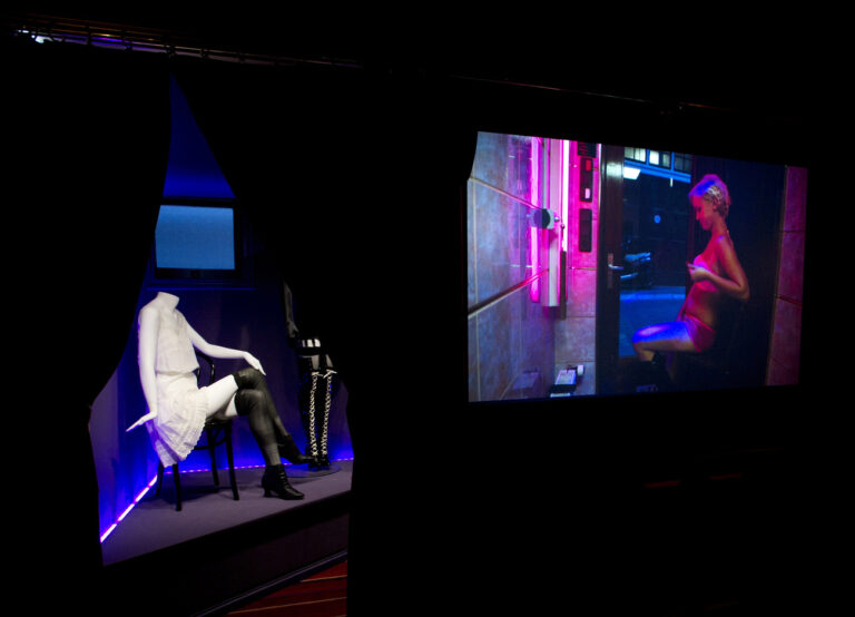 In this photo taken Tuesday, Feb. 4, 2014, a film showing prostitutes in their daily lives, right, and clothes prostitutes wore earlier in the 20th century, left, are shown at the 'Red Light Secrets' museum in Amsterdam. On any given evening, thousands of tourists stroll down the narrow streets of Amsterdam's famed Red Light District, gawking at ladies in lingerie who work behind windows, making a living selling sex for money. Now a small educational museum is opening in heart of the district that aims to show reality from the other side of the glass. Organizer Melcher de Wind says the Red Light Secrets museum is for those who want to learn more about how the area works without actually visiting a prostitute. (AP Photo/Evert Elzinga)