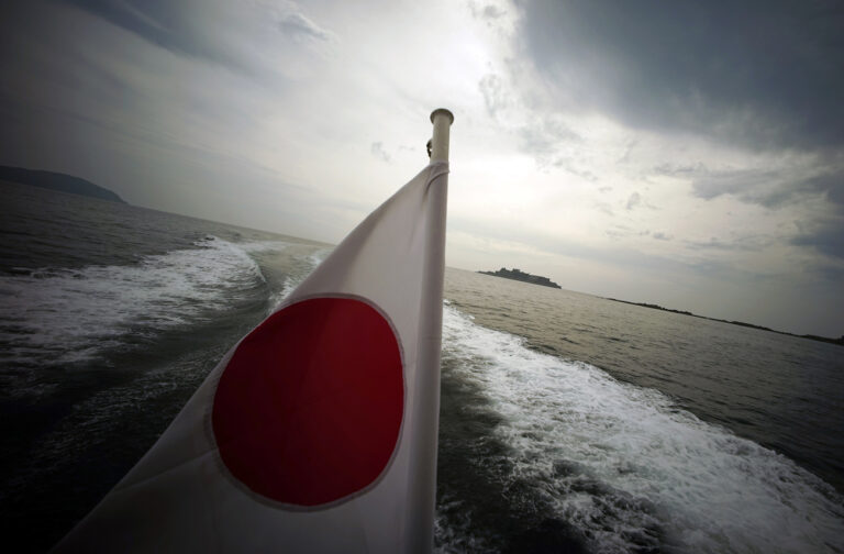 In this June 29, 2015 photo, a Japanese flag is hoisted on a tourist boat as Hashima Island, commonly known as Gunkanjima, which means “Battleship Island,” is seen off Nagasaki, Nagasaki Prefecture, southern Japan. The island is one of 23 old industrial facilities seeking UNESCO's recognition as world heritage “Sites of Japan's Meiji Industrial Revolution” meant to illustrate Japan's rapid transformation from a feudal farming society into an industrial power at the end of the 19th century. UNESCO's World Heritage Committee is expected to approve the proposal during a meeting being held in Bonn, Germany, through July 9. (AP Photo/Eugene Hoshiko)
