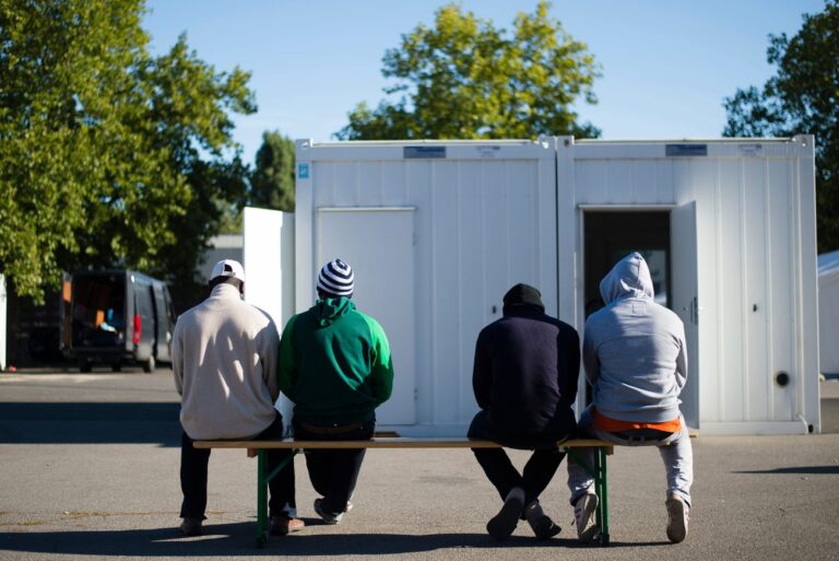 epa04921694 Four men wait to be registered in front of a LaGeSo (State Office for Health and Social Services) container, at the refugee shelter in the former Schmidt-Knobelsdorf barracks in Berlin, Germany, 09 September 2015. Chancellor Angela Merkel tempered Germany's welcome to hundreds of thousands of refugees from war and persecution with a warning 09 September that migrant communities must integrate into German life. The chancellor this week announced 6 billion euros (6.6 billion dollars) in extra spending to accommodate as many as 800,000 asylum seekers expected to arrive this year. EPA/GREGOR FISCHER