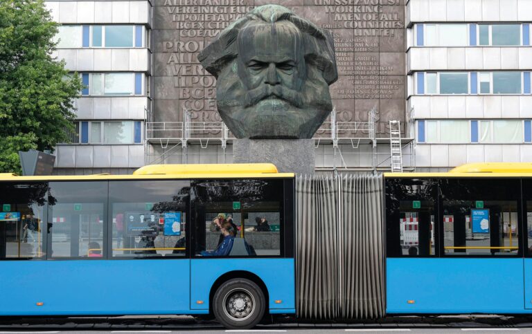 2T2K2RE DEUTSCHLAND, Sachsen, Chemnitz, in DDR Zeiten ehemals Karl-Marx-Stadt, Karl-Marx-Monument, die 7,1 m hohe und ca. vierzig Tonnen schwere Plastik, wurde nach einem Entwurf des sowjetischen Kunstlers Lew Kerbel realisiert und 1971 eingeweiht, Hintergrund Hauswandrelief mit Slogan Proletarier aller Lander vereinigt Euch aus Marx Schrift Kommunistisches Manifest in verschiedenen Sprachen