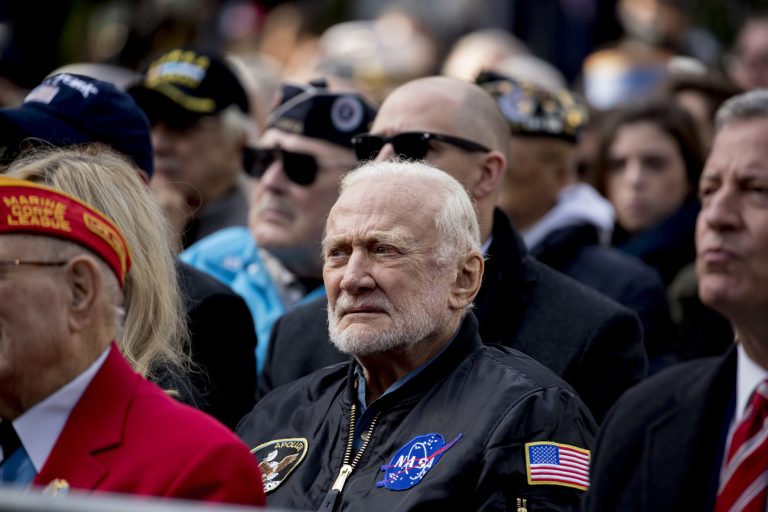 Apollo 11 astronaut Buzz Aldrin, center, and New York Mayor Bill de Blasio, right, sit in the audience as President Donald Trump speaks at a wreath laying ceremony at the New York City Veterans Day Parade at Madison Square Park, in Washington, Monday, Nov. 11, 2019. (AP Photo/Andrew Harnik)