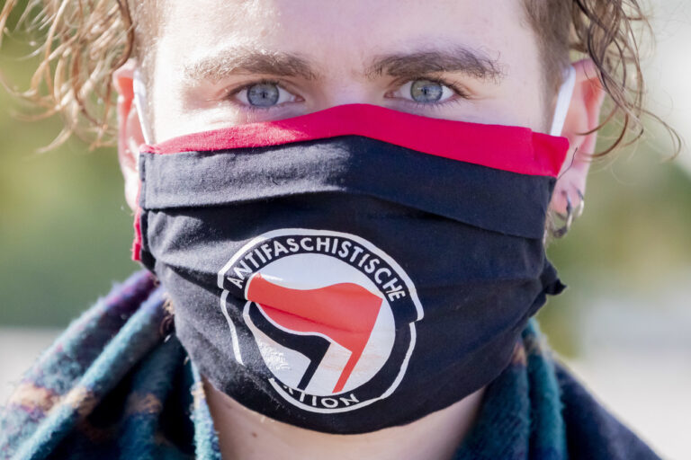 03.10.2020, Brandenburg, Potsdam: Ein Mann mit Antifa-Maske schaut bei einer Kundgebung der Protestinitiative «Re:Kapitulaition» gegen die Einheitsfeierlichkeiten in die Kamera. Potsdam als Brandenburger Landeshauptstadt ist in diesem Jahr Gastgeber der zentralen Feierlichkeiten zum Tag der Deutschen Einheit. Foto: Christoph Soeder/dpa +++ dpa-Bildfunk +++ (KEYSTONE/DPA/Christoph Soeder)