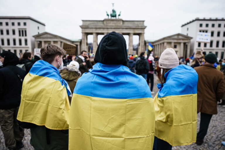 epa09780725 People wear the Ukrainian national flag on their shoulders during a protest against Russia's military operation in Ukraine, in front of the Brandenburg Gate in Berlin, Germany, 24 February 2022. Russian troops entered Ukraine on 24 February prompting the country's president to declare martial law. EPA/CLEMENS BILAN