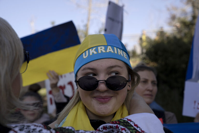 A woman is assisted with a head covering in the colors of the Ukrainian flag at protest Russia's against invasion of Ukraine outside of the Knesset, Israel's parliament, in Jerusalem, Monday, Feb. 28, 2022. (AP Photo/Maya Alleruzzo)