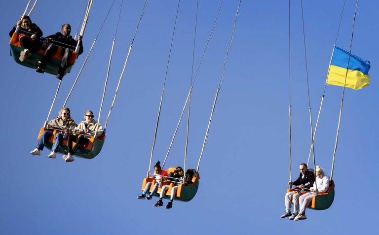 epa09834107 A Ukrainian flag waves as refugees sit in a leisure ride as they spend a day at the fun fair in Westerpark in Amsterdam, Netherlands, 18 March 2022. Fair operator Frans Stuy offers refugees from Ukraine this day to relax and enjoy. EPA/Koen van Weel