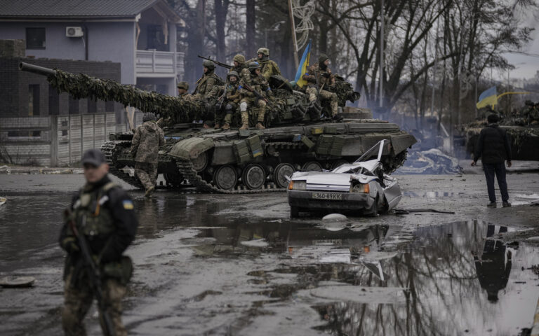 A man stands next to a civilian vehicle that was destroyed during fighting between Ukrainian and Russian forces that still contains the dead body of the driver as Ukrainian servicemen ride on a tank vehicle outside Kyiv, Ukraine, Saturday, April 2, 2022. As Russian forces pull back from Ukraine's capital region, retreating troops are creating a 