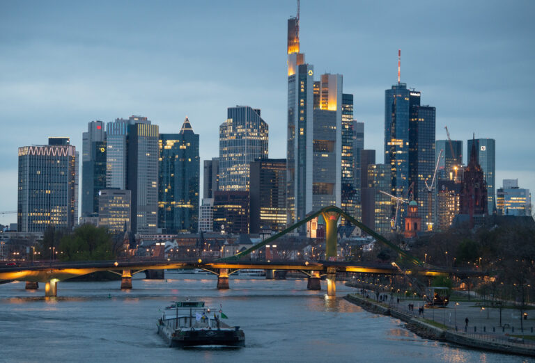 ARCHIV - 06.04.2022, Hessen, Frankfurt/Main: Binnenschiffe fahren im letzten Licht des Tages vor der Bankenskyline der Innenstadt über den Main. Trotz steigender Zinsen im Euroraum erheben weiterhin mehrere Dutzend Kreditinstitute Negativzinsen auf dem Tagesgeld- oder Girokonto. (zu dpa 