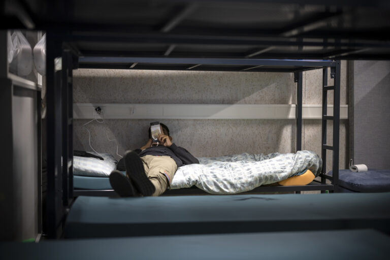 Ein Mann benutzt sein Mobiltelefon waehrend er in einem Schlafsaal auf einem Bett liegt, aufgenommen waehrend eines Medienrundgans im Bundesasylzentrum Zuerich, am Donnerstag, 27. Oktober 2022 in Zuerich. (KEYSTONE/Michael Buholzer)