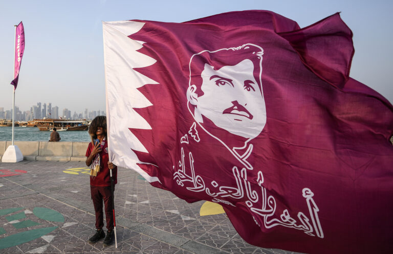 A Qatar fan holds a flag showing the Emir of Qatar Tamim bin Hamad Al Thani at the Doha Corniche on the day before the start of the Soccer World Cup in Doha, Qatar, Saturday, Nov. 19, 2022. (AP Photo/Martin Meissner)