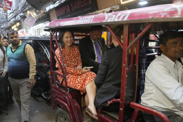 A man looks on as German Foreign Minister Annalena Baerbock, center, rides on an e-rickshaw during her tour of Chandni Chowk, in the old quarters of New Delhi, India, Monday, Dec. 5, 2022. (AP Photo/Manish Swarup)
