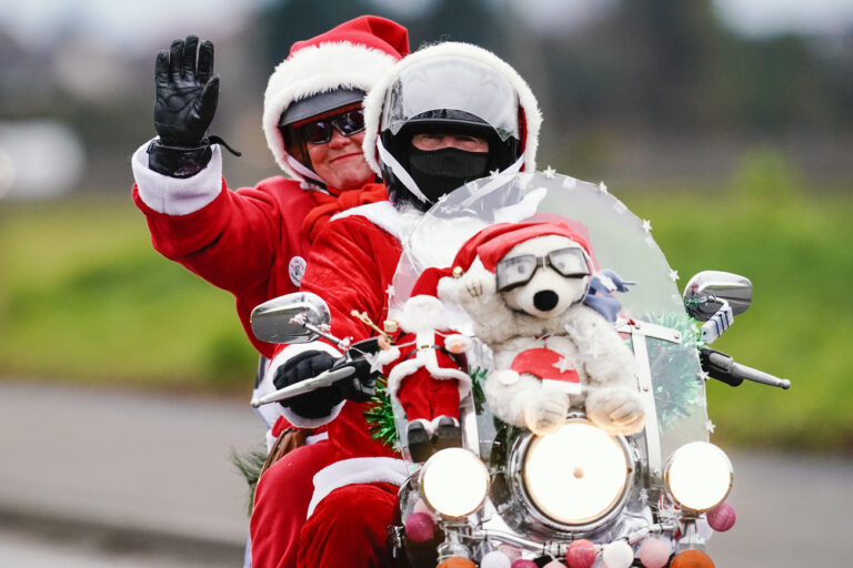 06.12.2022, Rheinland-Pfalz, Kuhardt: Als Weihnachtsmänner verkleidete Motorradfahrer fahren winkend über eine Landstraße. Die Motorradfahrer sind im südlichen Rheinland-Pfalz auf Spendentour für ein Kinderhospiz. Im vergangenen Jahr sammelten die 