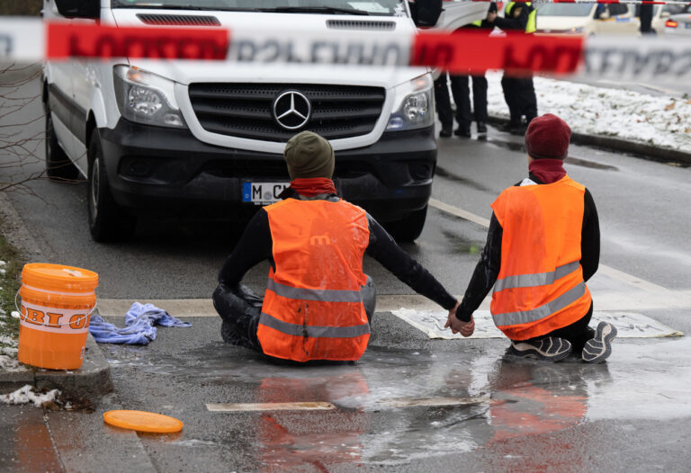 ARCHIV - 14.12.2022, Bayern, München: Zwei Klimaaktivisten nehmen an einer Protestaktion der Gruppe Letzte Generation teil, indem sie versuchen sich auf einer Strasse trotz Nieselregen und Minusgraden festzukleben. Die Aktion fand trotz einer Allgemeinverfügung der Stadt München zu Klimaprotesten statt. (zu dpa: «Letzte Klimaaktivisten in Bayern aus Präventivgewahrsam entlassen») Foto: Peter Kneffel/dpa +++ dpa-Bildfunk +++ (KEYSTONE/DPA/Peter Kneffel)