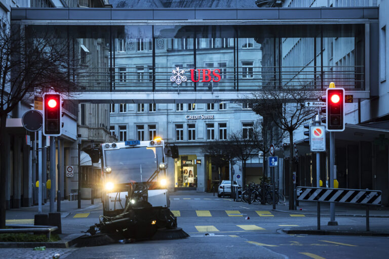 A cleaning vehicle collects garbage past logos of the Swiss banks Credit Suisse and UBS in Zurich, Switzerland on Sunday March 19, 2023. (KEYSTONE/Michael Buholzer).