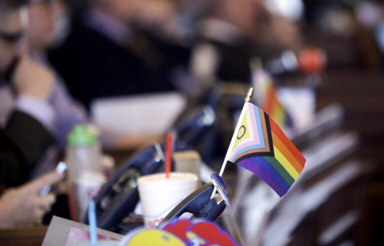 FILE - A flag supporting LGBTQ+ rights decorates a desk on the Democratic side of the Kansas House of Representatives during a debate, March 28, 2023, at the Statehouse in Topeka, Kan. Schools and colleges across the U.S. would be forbidden from enacting outright bans on transgender athletes under a proposal released Thursday, April 6, from the Biden administration, but teams could create some limits in certain cases, for example, to ensure fairness. The proposed rule sends a political counterpunch toward a wave of Republican-led states that have sought to ban trans athletes from competing in school sports that align with their gender identities. (AP Photo/John Hanna, File)