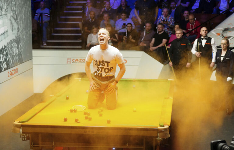 A 'Just Stop Oil' protester jumps on the table and throws orange powder during the match between Robert Milkins against Joe Perry as part of day three of the Cazoo World Snooker Championship at the Crucible Theatre, Sheffield, Britain, Monday, April 17, 2023. (Mike Egerton/PA via AP)