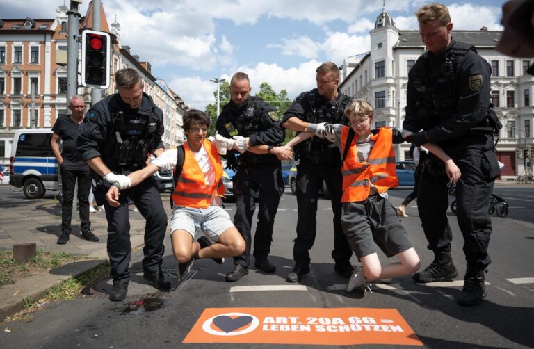 04.07.2023, Sachsen, Leipzig: Polizeibeamte heben zwei Klimaaktivisten der Gruppe «Letzte Generation» von einer Straße. Nur wenige Minuten nach dem Freispruch für fünf Mitglieder der «Letzten Generation» vom Vorwurf der Nötigung haben die Klimaaktivisten eine Hauptverkehrsstraße blockiert. Zehn Frauen und Männer setzten sich auf eine Kreuzung und protestierten gegen die Folgen der Klimakrise. Foto: Hendrik Schmidt/dpa +++ dpa-Bildfunk +++ (KEYSTONE/DPA/Hendrik Schmidt)