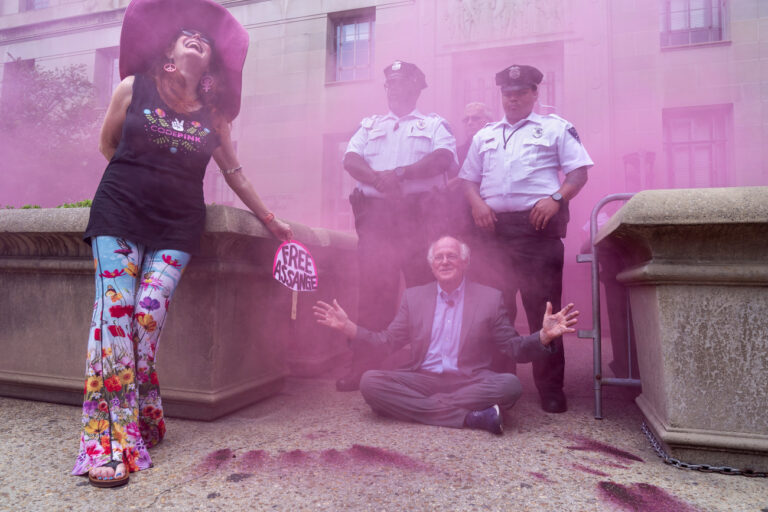 Jodie Evans, left, co-founder of protest group CODEPINK, reacts as Ben Cohen, co-founder of Ben & Jerry's, gestures through clearing pink smoke during a protest as he blocks the entrance to the Justice Department, during a protest of the prosecution of Wikileaks founder Julian Assange, Thursday, July 6, 2023, outside the Justice Department in Washington. (AP Photo/Jacquelyn Martin)