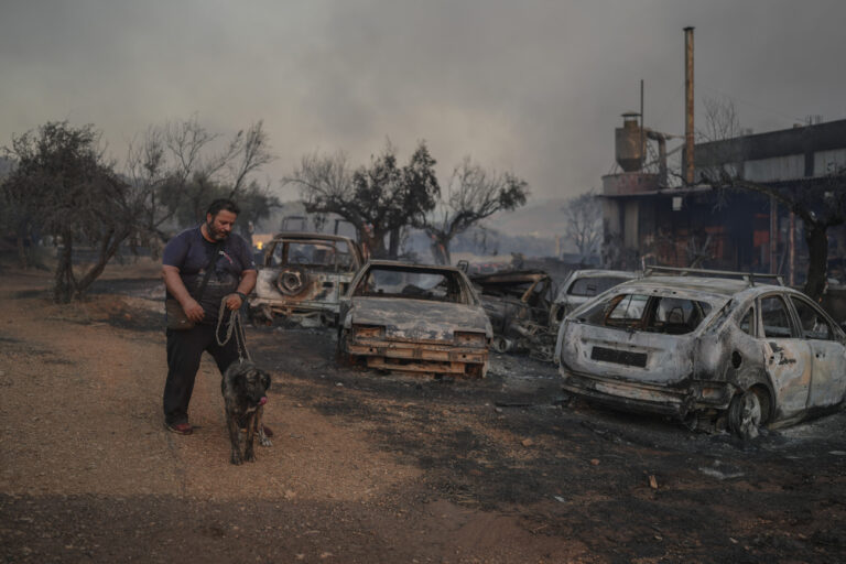 Thanassis Barberakis walks with his dog at his family shipyard damaged from the fire in Mandra west of Athens, on Tuesday, July 18, 2023. In Greece, where a second heatwave is expected to hit Thursday, three large wildfires burned outside Athens for a second day. Thousands of people evacuated from coastal areas south of the capital returned to their homes Tuesday when a fire finally receded after they spent the night on beaches, hotels and public facilities. (AP Photo/Petros Giannakouris)