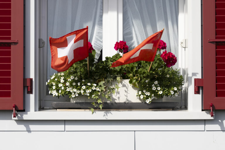 Zwei Schweizer Flaggen wehen in einem Geranientopf auf einem Fensterbrett, am Montag, 31. Juli 2023 in Studen. (KEYSTONE/Peter Klaunzer)