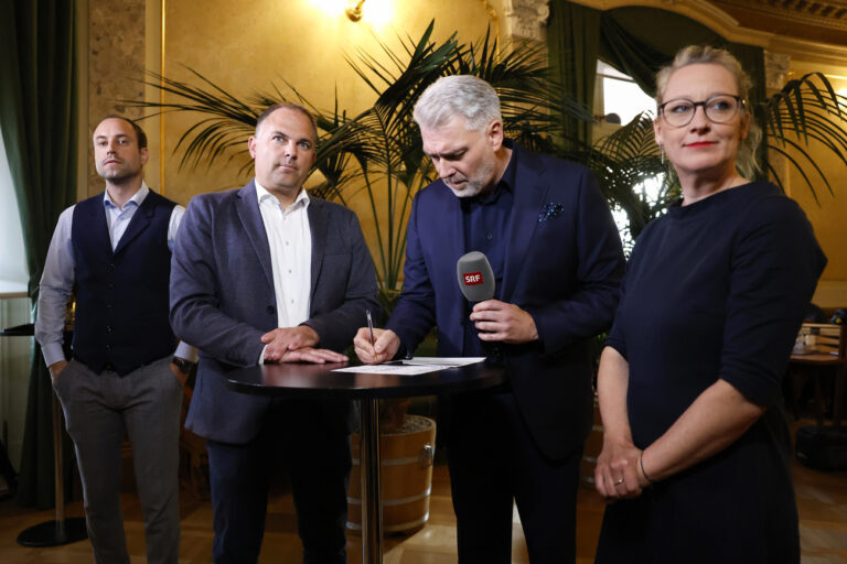 Aline Trede, Nationalraetin GP-BE, Moderator Sandro Brotz, Marcel Dettling, Nationalrat SVP-SZ und Wahlkampfleiter SVP, und Christian Wasserfallen, Nationalrat FDP-BE, von vorne, verfolgen die letzten Hochrechnungen vor einem TV-Interview in der Wandelhalle, am Wahltag der Eidgenoessischen Parlamentswahlen, am Sonntag, 22. Oktober 2023 im Bundeshaus in Bern. Die Schweizer Buergerinnen und Buerger waehlen das Bundesparlament mit den beiden Kammern Nationalrat und Staenderat. (KEYSTONE/Peter Klaunzer)