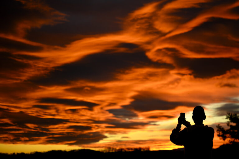 A person takes pictures with his smartphone of the sky illuminated during the sun set behind the Jura mountains in Gros-de-Vaud Region on christmas eve, in Daillens, Southwestern Switzerland, Sunday, December 24, 2023.(KEYSTONE/Laurent Gillieron)