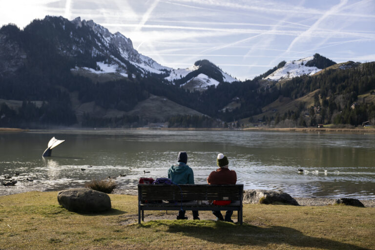 Zwei Personen sitzen auf einer Bank und geniessen die Sonne in Schwarzsee, Schweiz, am Samstag, 30. Dezember 2023. (KEYSTONE/Anthony Anex)
