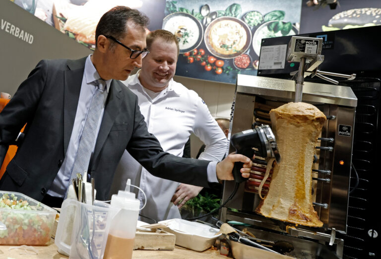 19.01.2024, Berlin: Cem Özdemir (Bündnis 90/Die Grünen), Bundesminister für Ernährung und Landwirtschaft, schneidet beim Eröffnungsrundgang über das Messegelände der Grünen Woche am Stand des Lebensmittelverbandes Deutschland Fleisch von einem Dönerspieß ab. Neben ihm steht Koch Adrian Springer. Vom 19. bis 28. Januar 2024 findet die 88. Ausgabe der Grünen Woche, der internationalen Leitmesse für Ernährung, Landwirtschaft und Gartenbau, statt. Foto: Carsten Koall/dpa +++ dpa-Bildfunk +++ (KEYSTONE/DPA/Carsten Koall)