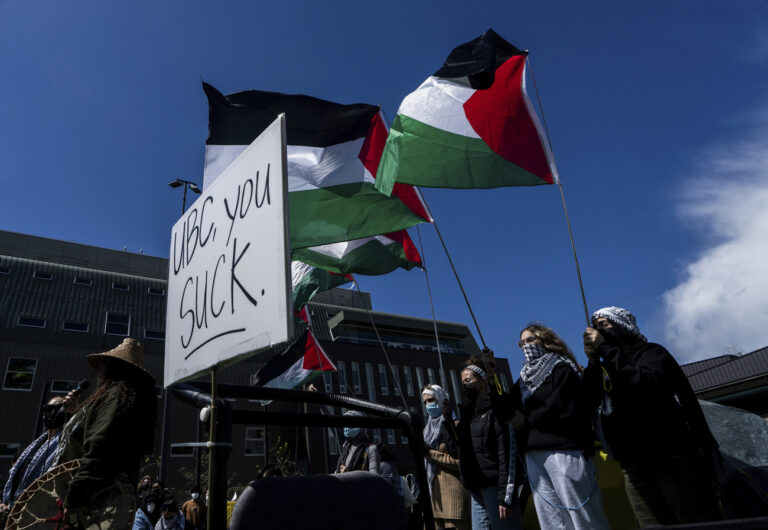 Pro-Palestinian supporters hold flags while standing behind someone speaking during a student encampment at the University of British Columbia campus in Vancouver, British Columbia, Monday, April 29, 2024. (Ethan Cairns/The Canadian Press via AP)