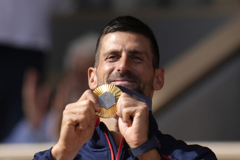 Serbia's Novak Djokovic shows his gold medal after defeating Spain's Carlos Alcaraz in the men's singles tennis final at the Roland Garros stadium during the 2024 Summer Olympics, Sunday, Aug. 4, 2024, in Paris, France. Djokovic has won his first Olympic gold medal by beating Alcaraz 7-6 (3), 7-6 (2) in the 2024 Games men's tennis singles final. (AP Photo/Manu Fernandez)