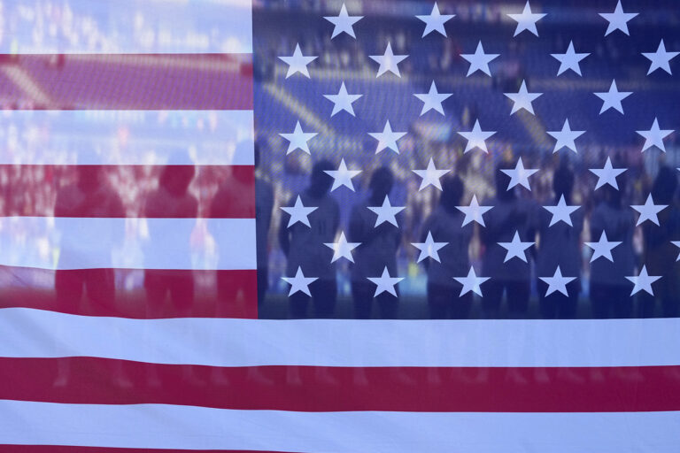 United States players are seen through an USA flag as they pose for a photo ahead of a women's semifinal soccer match between the United States and Germany at the 2024 Summer Olympics, Tuesday, Aug. 6, 2024, at Lyon Stadium in Decines, France. (AP Photo/Laurent Cipriani)