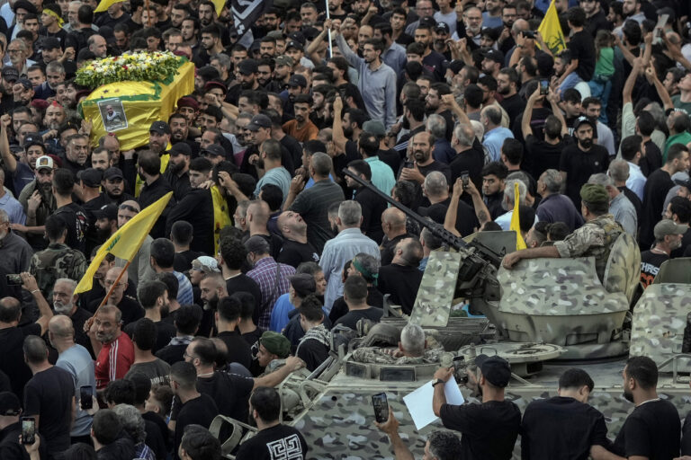 Lebanese army soldiers sit on their armoured vehicle as mourners carry the coffin of Mohammed Mahdi, son of Hezbollah legislator Ali Ammar, who was killed Tuesday after his handheld pager exploded, in the southern suburb of Beirut, Lebanon, Wednesday, Sept. 18, 2024. (AP Photo/Bilal Hussein)