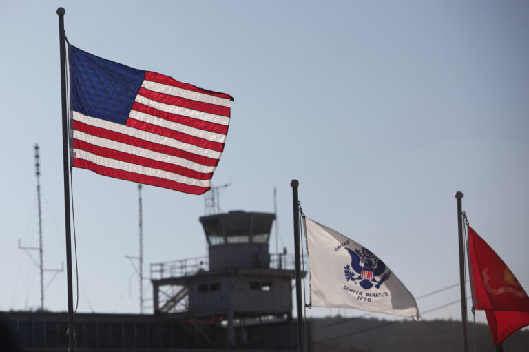 In this photo, reviewed by the U.S. Military, an American flag flies, with an old air-traffic control tower from a closed-down airport pictured in the background, at Camp Justice, the location of the U.S. Military Commissions court for war crimes, at the U.S. Naval Base, in Guantanamo Bay, Cuba, Monday, Jan. 19, 2009. Military judges in Guantanamo pressed forward Monday with hearings for five men accused of orchestrating the Sept. 11 attacks and for a Canadian accused of killing a U.S. soldier.(AP Photo/Brennan Linsley, Pool)