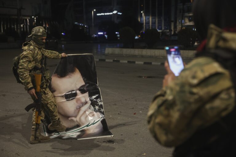 A Syrian opposition fighter takes a picture of a comrade stepping on a portrait of overthrown Syrian President Bashar Assad in Aleppo, early Saturday, Nov. 30, 2024. (AP Photo/Ghaith Alsayed)