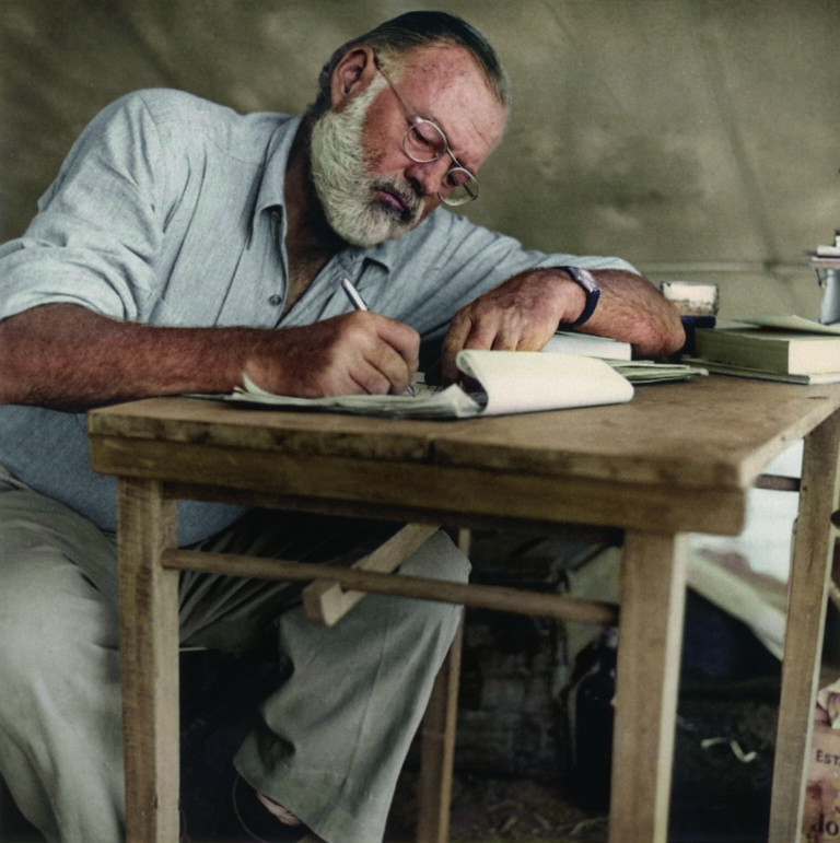2RP32JM Photograph of Ernest Hemingway sitting at a table writing while at his campsite in Kenya circa 1953.