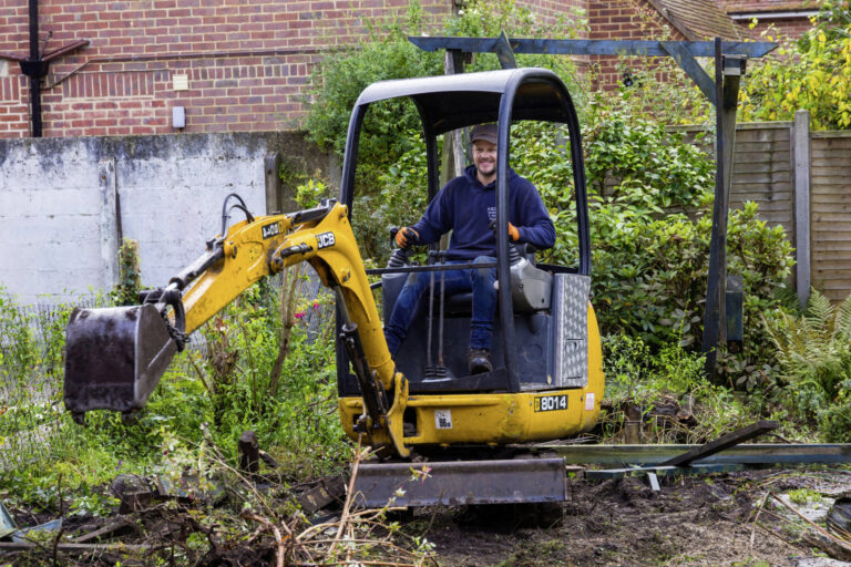 2D3NCR9 Garden clearance work and renovation taking part in garden at Bournemouth, Dorset UK in October - worker operating jcb mini excavator digger